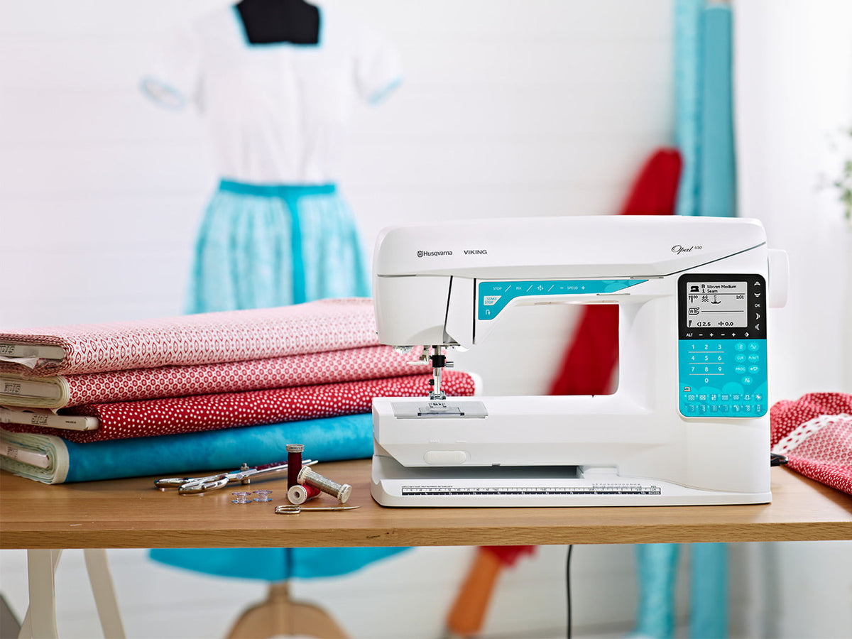 Husqvarna Viking Opal 650 sewing machine on a table beside folded fabrics
