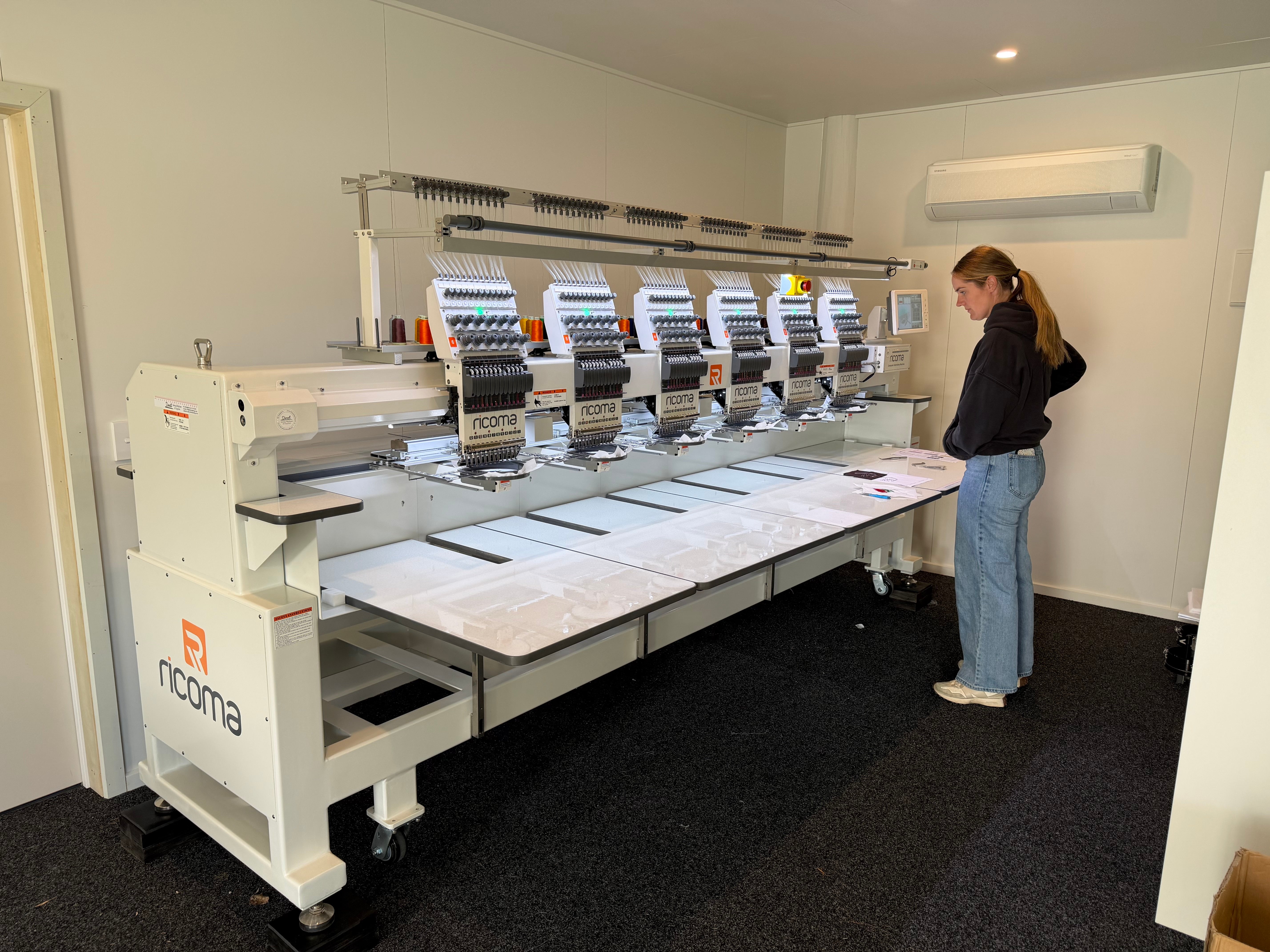 Nicole standing beside Naninama Embroidery's newly installed six-head Ricoma embroidery machine in Alexandra